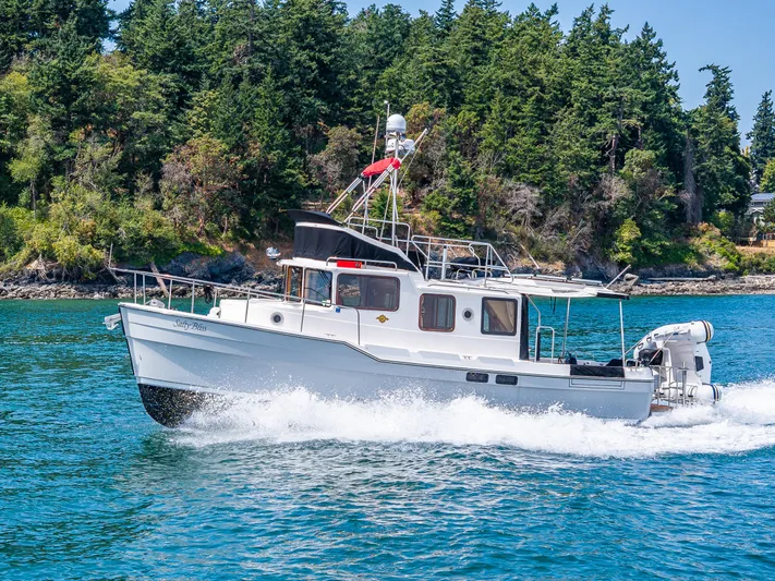 Salty Bliss Yacht Photos Pics 2021 Ranger Tugs R-31 CB cruising on blue water near a forested shoreline.