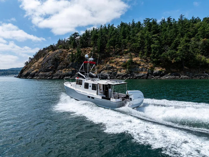 Salty Bliss Yacht Photos Pics 2021 Ranger Tugs R-31 CB cruising near a forested coastline under a partly cloudy sky.