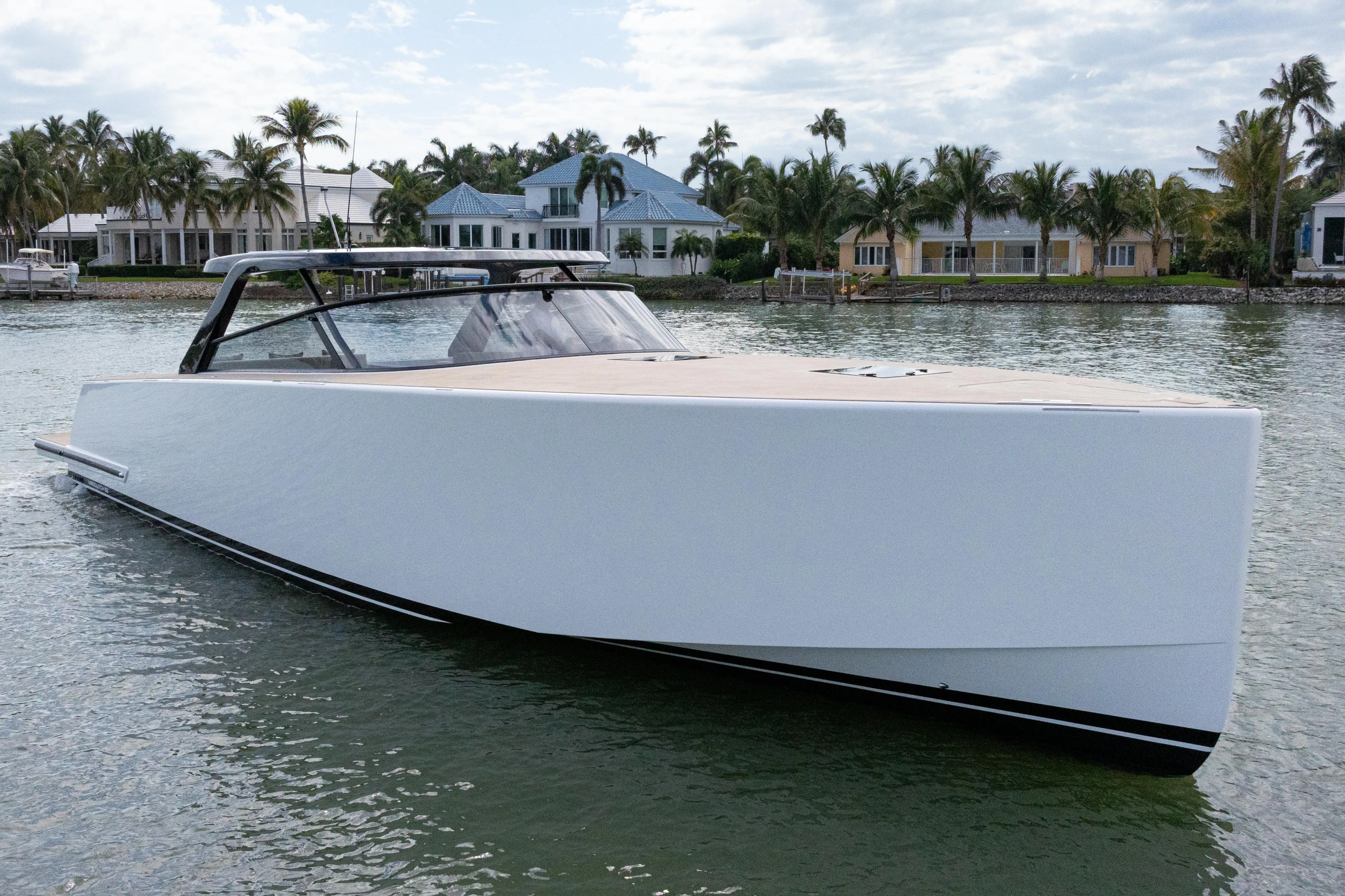 2024 VanDutch 56 yacht on serene water, with luxury waterfront homes in the background.