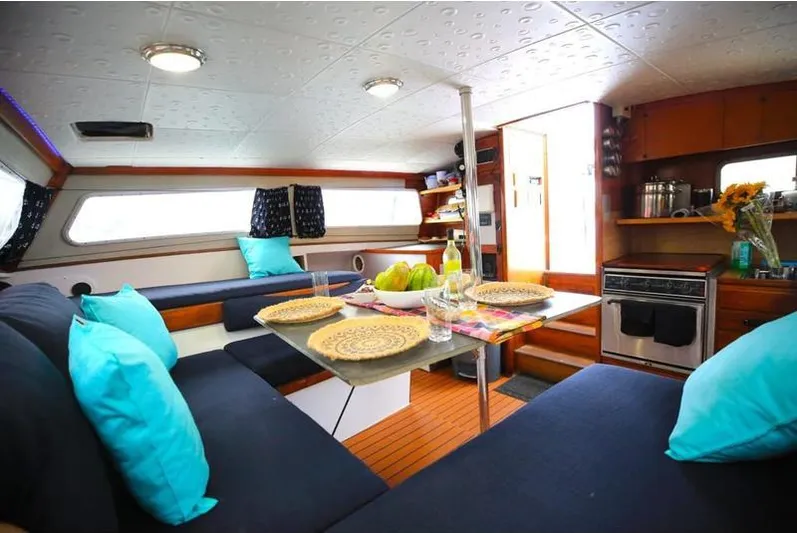 Hiolani II Yacht Photos Pics Cozy 1988 CSK Polycon yacht interior with dining area, blue cushions, and kitchen amenities.