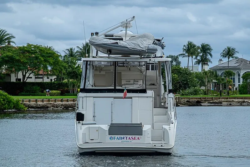 Faintasea Yacht Photos Pics 2000 Silverton 442 Cockpit Motor Yacht on water, surrounded by lush greenery and palm trees.