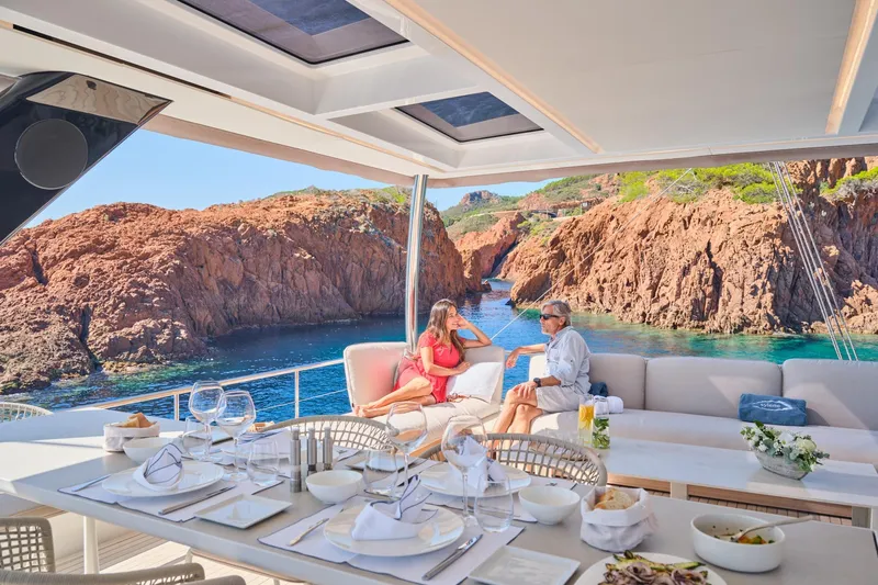  Yacht Photos Pics Luxury Lagoon Seventy 7 yacht with elegant dining setup, scenic rocky coastline view, 2023 model.