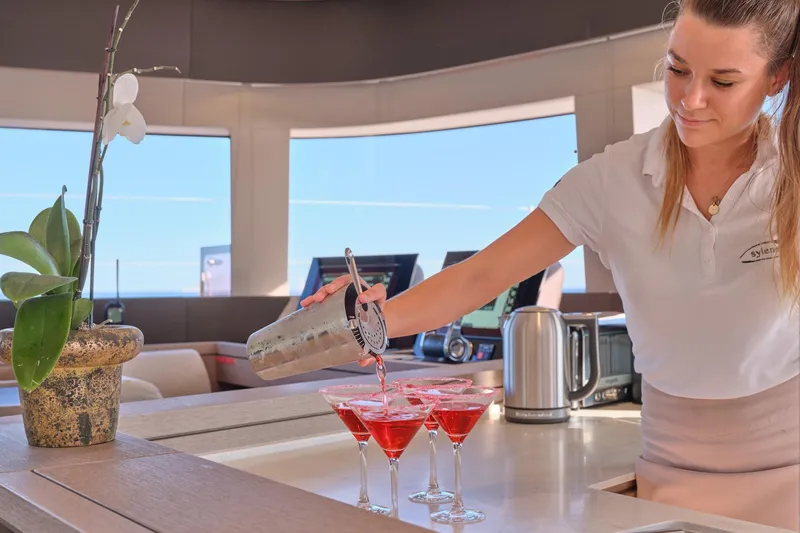  Yacht Photos Pics Bartender serving cocktails on 2023 Lagoon Seventy 7 yacht, elegant interior setting.