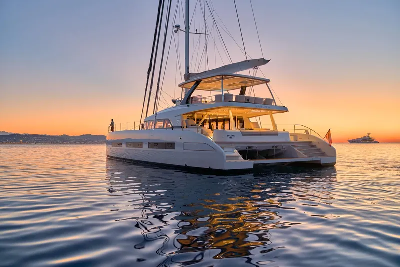  Yacht Photos Pics 2023 Lagoon Seventy 7 yacht at sunset, reflecting on calm ocean waters.