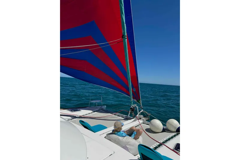 Apres-sea Yacht Photos Pics Man relaxing on Lagoon 380 S2 catamaran with colorful sail, 2012 model, on open sea.