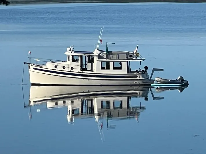 Rafiki Yacht Photos Pics Nordic Tug 37 (2000) reflecting on calm water, showcasing classic design and serene setting.