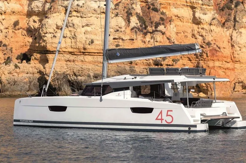  Yacht Photos Pics 2025 Fountaine Pajot Elba 45 catamaran sailing near rocky cliffs.
