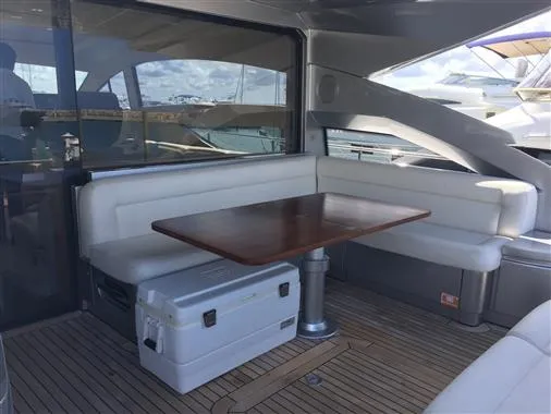 Luxurious seating area on a 2010 Pershing 64' yacht with wooden table and white cushions.