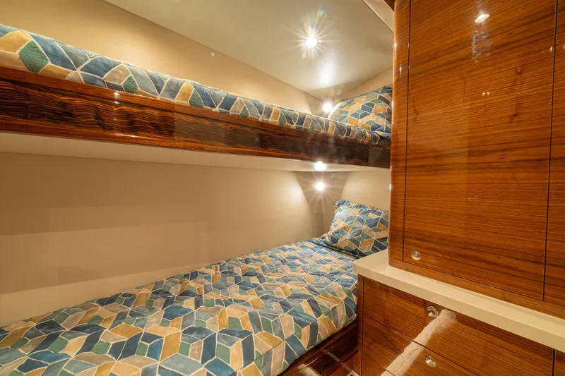  Yacht Photos Pics 2022 Jarrett Bay Flybridge Express cabin with wooden finish and geometric-patterned bunk beds.