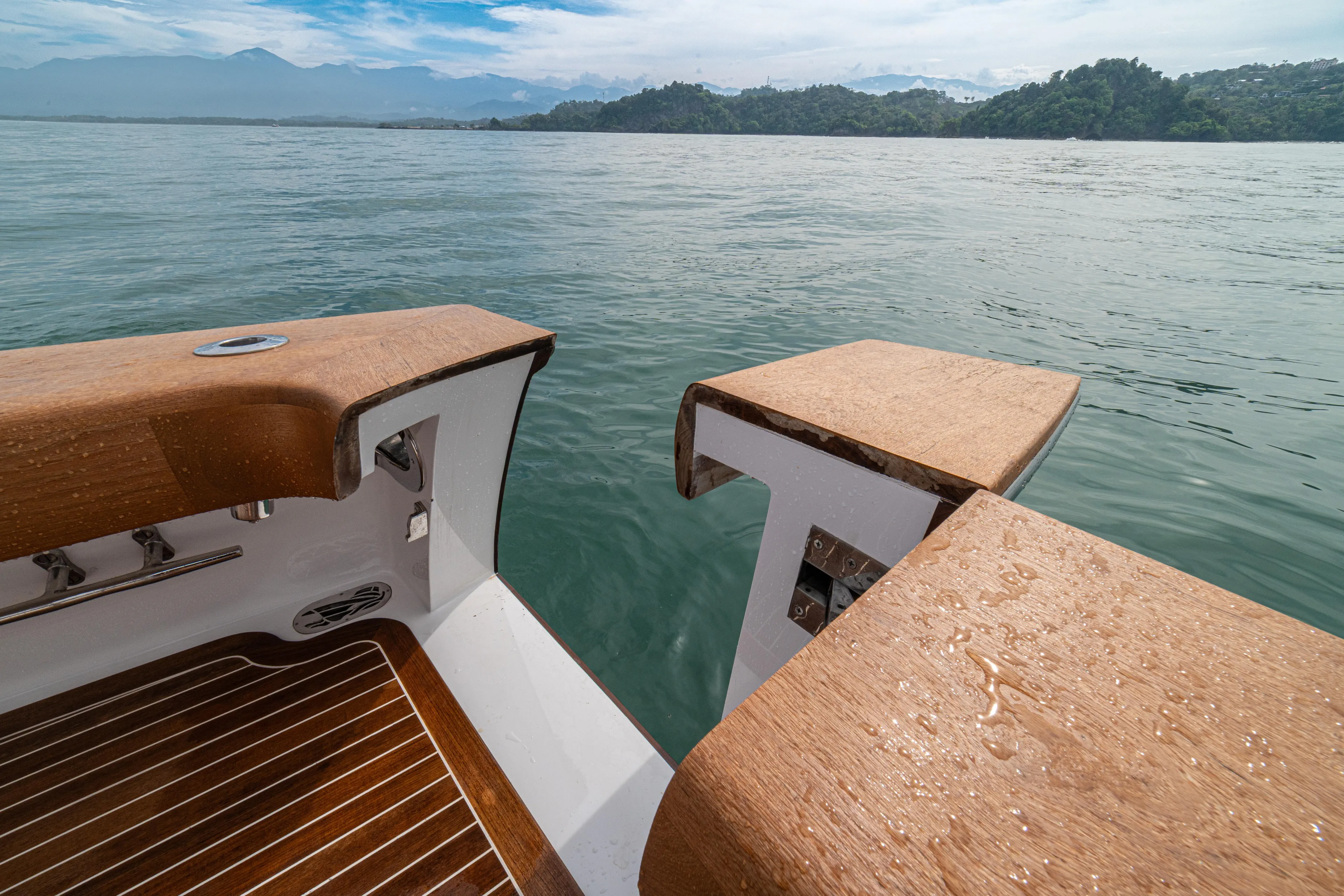  Yacht Photos Pics 2022 Jarrett Bay Flybridge Express boat with wooden deck, overlooking serene waters and distant hills.