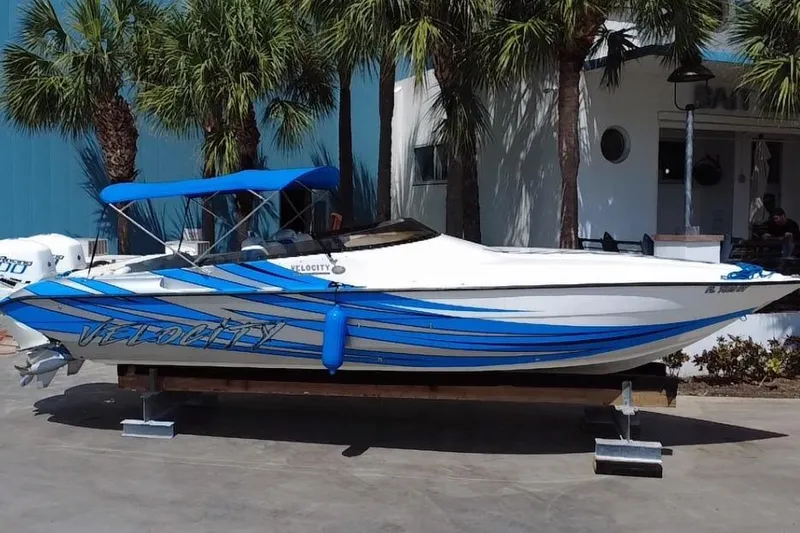  Yacht Photos Pics 2021 Velocity 290sc speedboat with blue stripes, docked near palm trees.