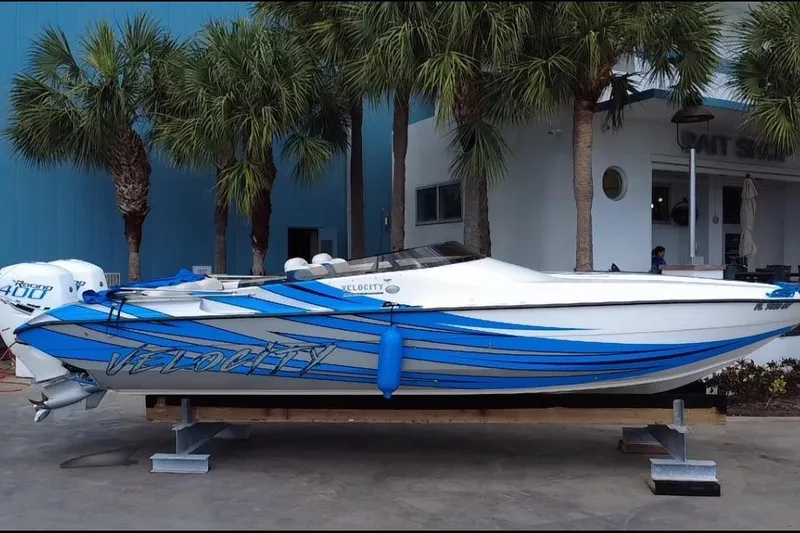  Yacht Photos Pics 2021 Velocity 290sc speedboat with blue stripes, docked near palm trees.
