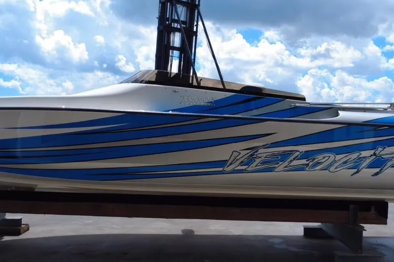  Yacht Photos Pics 2021 Velocity 290sc speedboat with blue stripes against a cloudy sky backdrop.