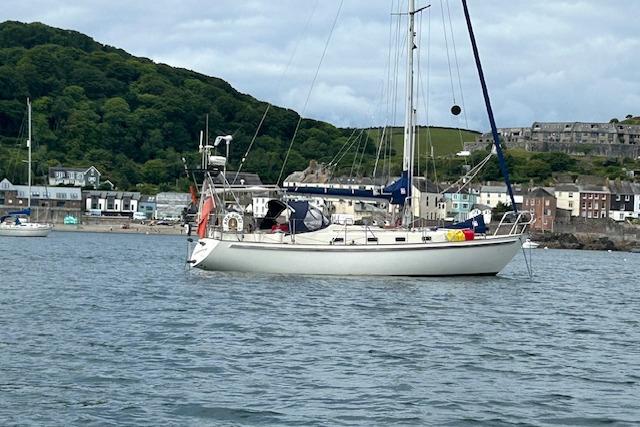 Sailboat "Rival 36" from 1995 anchored near coastal town with lush greenery.