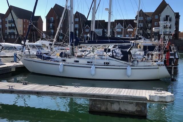 Sailboat docked in marina, Rival 36 model, 1995, with waterfront buildings in background.