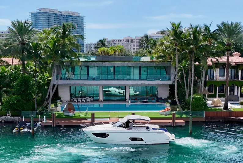  Yacht Photos Pics Luxury yacht Absolute 40 cruising by a modern waterfront mansion, surrounded by palm trees.