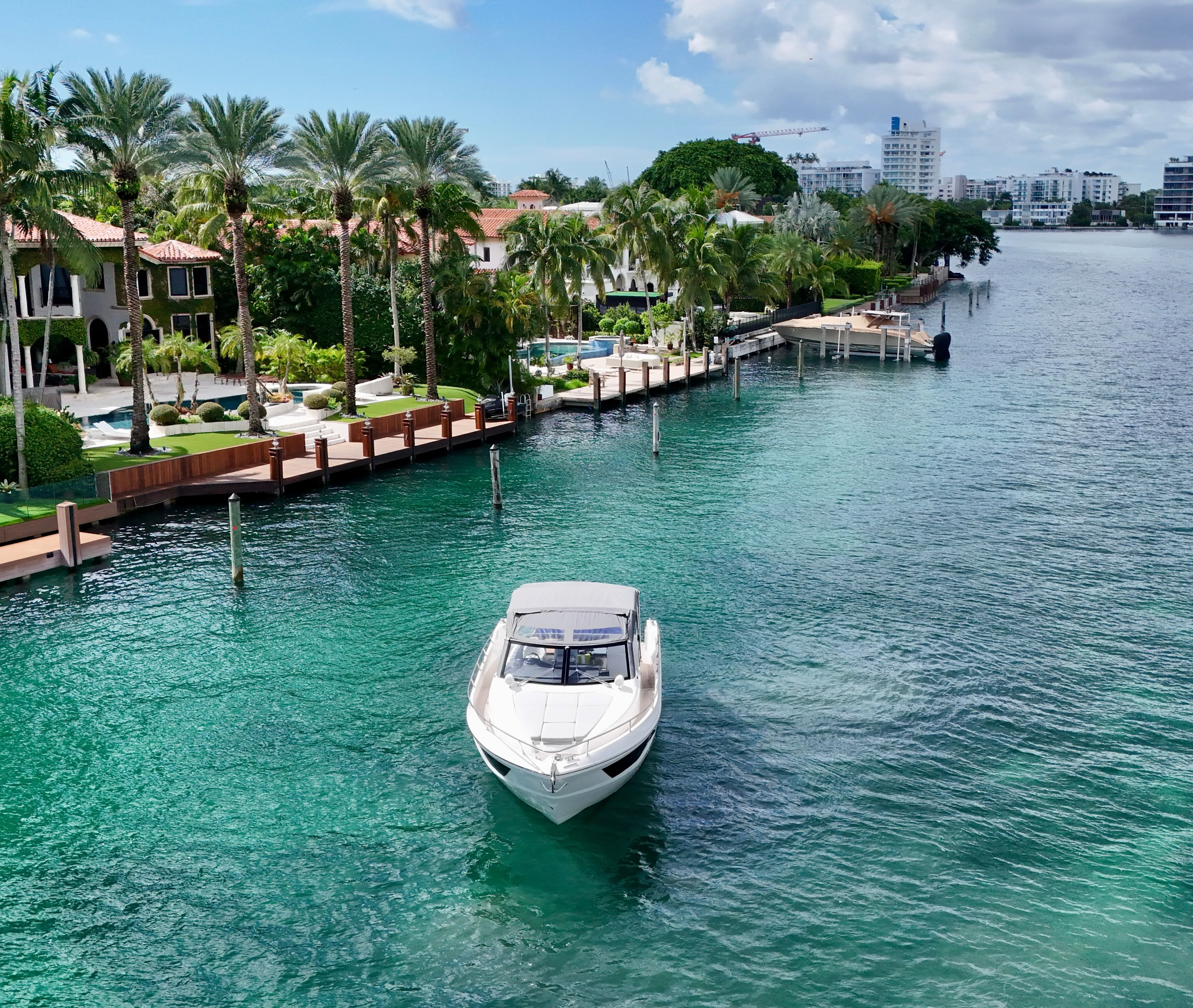  Yacht Photos Pics Luxury yacht cruising near waterfront homes, surrounded by palm trees and clear blue water.