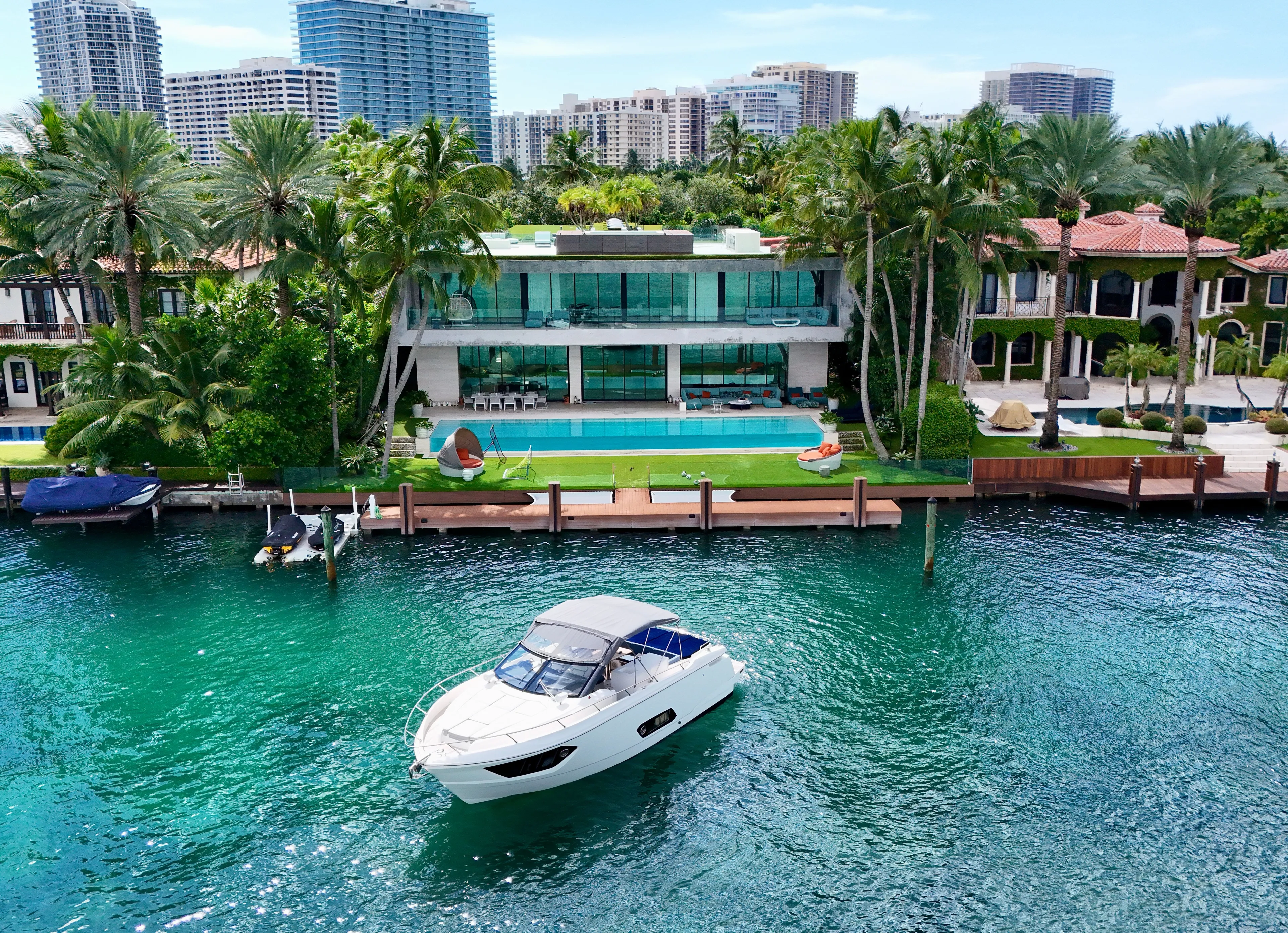  Yacht Photos Pics Luxury yacht cruising near waterfront mansion with palm trees and modern architecture.