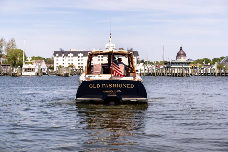 Old Fashioned Yacht Photos Pics Hinckley Picnic Boat EP 2002 on water, Annapolis backdrop, American flag displayed.