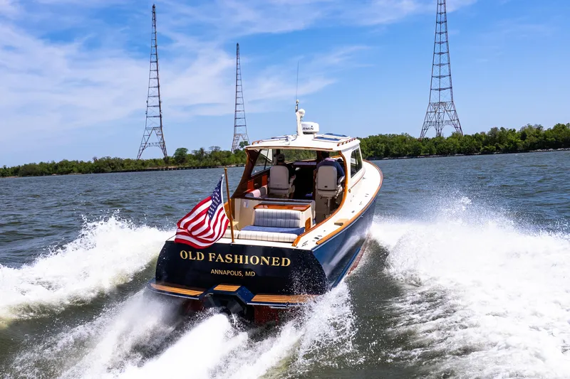 Old Fashioned Yacht Photos Pics Hinckley Picnic Boat EP 2002 cruising on water, American flag waving, clear sky background.