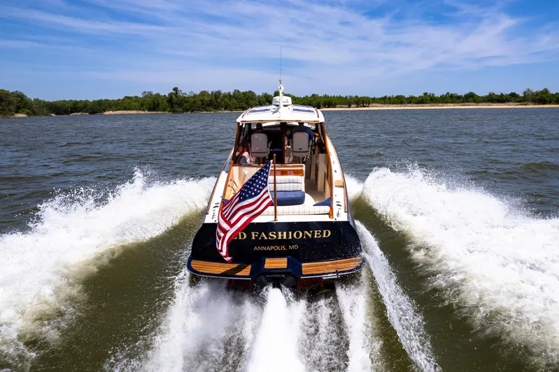Old Fashioned Yacht Photos Pics Hinckley Picnic Boat EP 2002 cruising on water with American flag, scenic background.
