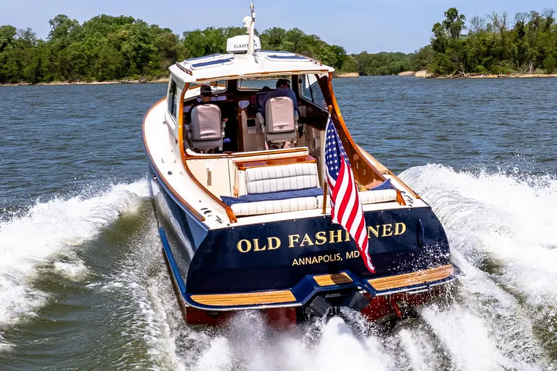 Old Fashioned Yacht Photos Pics 2002 Hinckley Picnic Boat EP cruising on water, displaying American flag, rear view.