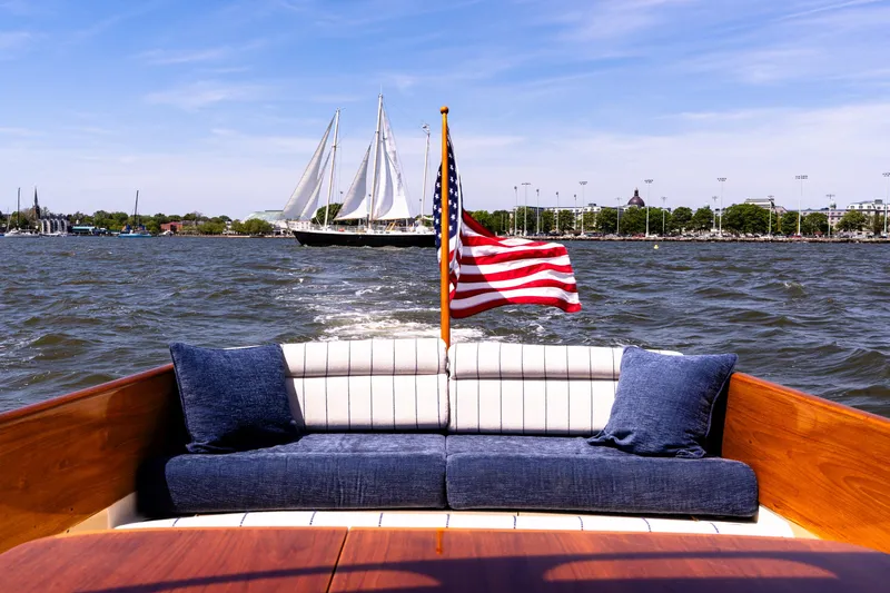 Old Fashioned Yacht Photos Pics Hinckley Picnic Boat EP 2002 cruising with American flag, sailboat in background, sunny day.