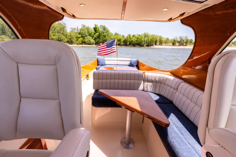 Old Fashioned Yacht Photos Pics 2002 Hinckley Picnic Boat EP interior with seating, table, and American flag on a sunny day.