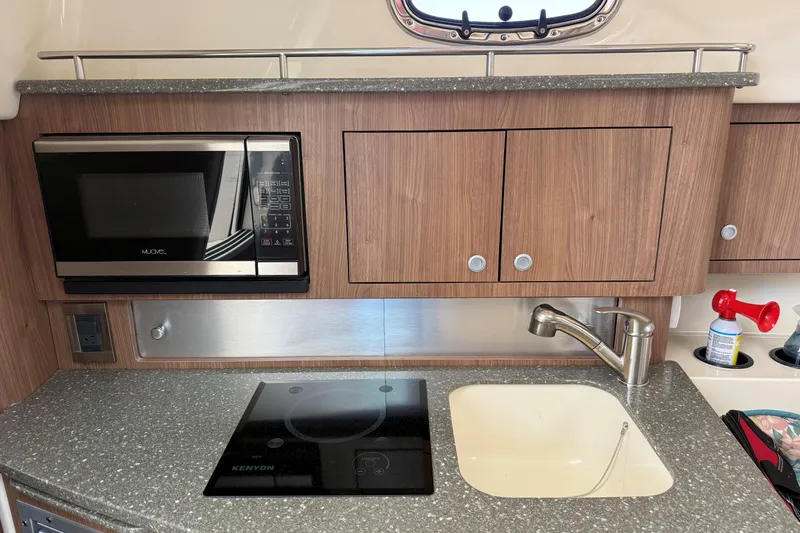  Yacht Photos Pics 2019 Boston Whaler 315 Conquest kitchen with microwave, stove, sink, and wooden cabinets.