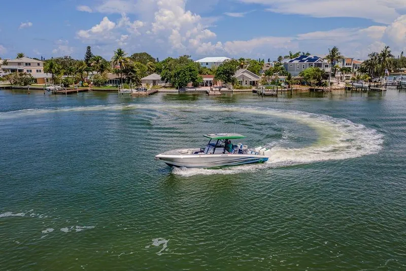  Yacht Photos Pics 2022 Fountain 34 SC boat cruising on a scenic waterfront with houses and palm trees.