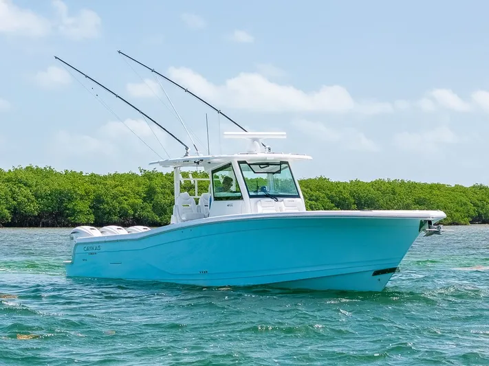 Caymas Yacht Photos Pics 2023 Caymas 401CC boat on water, featuring sleek design and fishing rods, with lush greenery background.