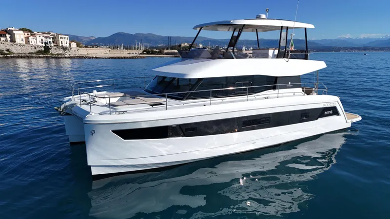 Barcajack Yacht Photos Pics 2022 Fountaine Pajot MY6 yacht on calm blue water near a coastal town.
