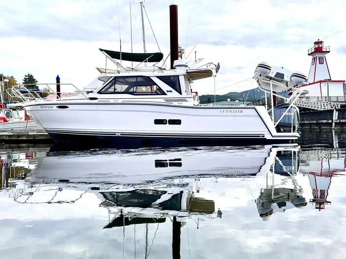 Yacht Photos Pics 2025 Cutwater C-288 Coupe boat docked near a lighthouse, reflecting on calm water.