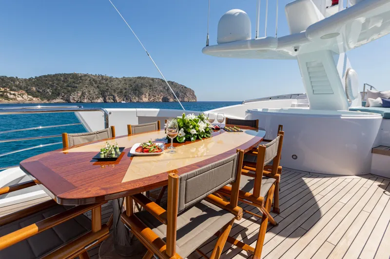 Benita Blue Yacht Photos Pics Luxurious dining setup on 2005 Evolution Yachts Custom, overlooking serene ocean and cliffs.