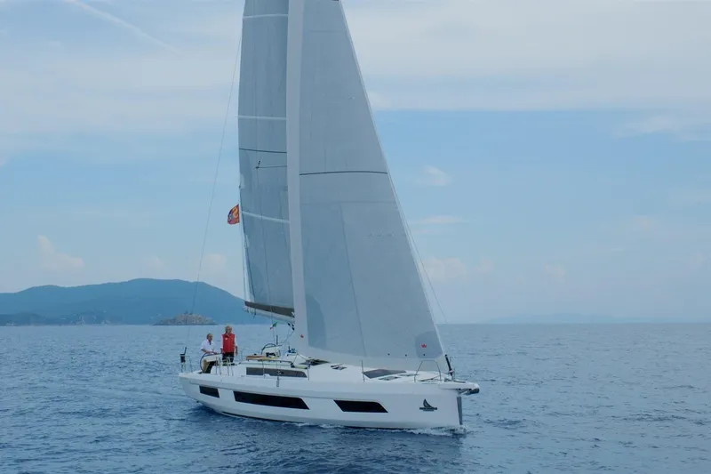  Yacht Photos Pics 2024 Dufour 44 sailboat cruising on open sea with scenic mountain backdrop.