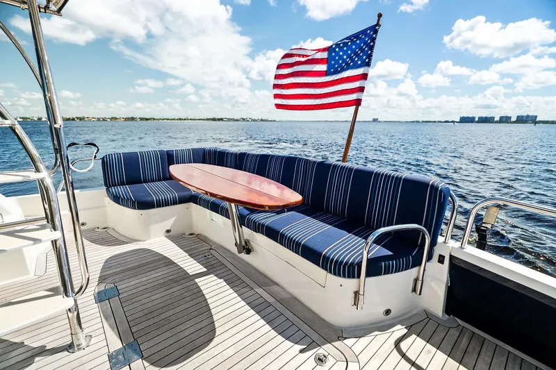 Highlander Yacht Photos Pics 2019 Sabre Flybridge yacht deck with striped seating and American flag, overlooking serene waters.