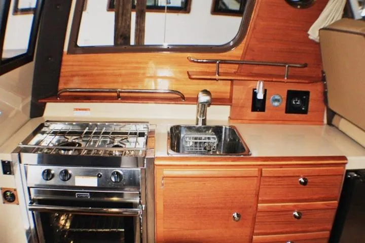Knot Working Yacht Photos Pics 2020 Ranger Tugs R-27 boat kitchen with stove, sink, and wooden cabinetry.