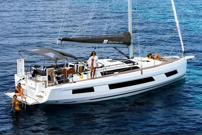  Yacht Photos Pics 2024 Dufour 44 yacht sailing with people relaxing on deck in clear blue waters.
