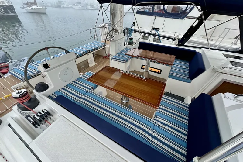 Pain Killer Yacht Photos Pics 2020 Bavaria C50 yacht cockpit with striped seating and wooden table, docked in a marina.