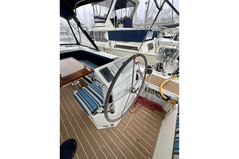 Pain Killer Yacht Photos Pics Steering wheel of a 2020 Bavaria C50 yacht with striped seating and nautical equipment.