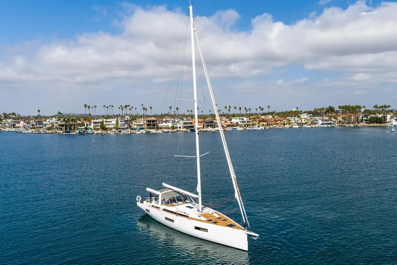 Joy Yacht Photos Pics 2023 Beneteau Oceanis Yacht 60 sailing near coastal homes under a blue sky.