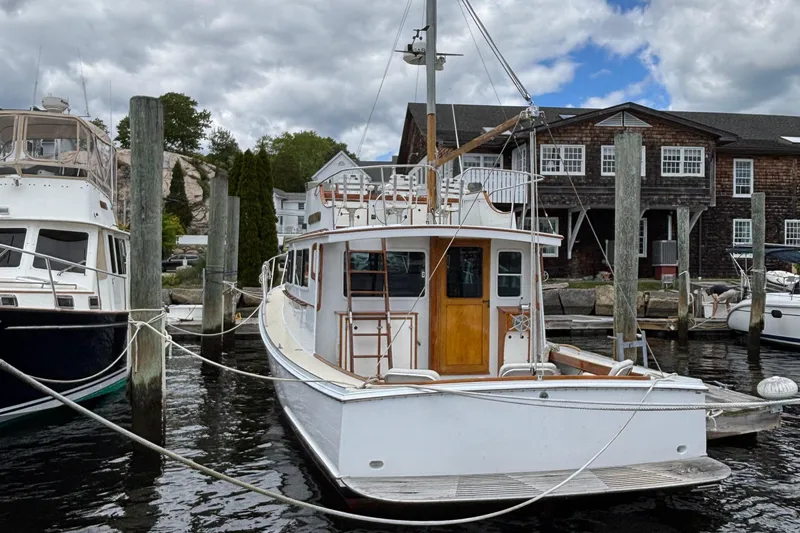 Carroll L Yacht Photos Pics White Lowell 40 boat docked at marina, cloudy sky, wooden building in background.