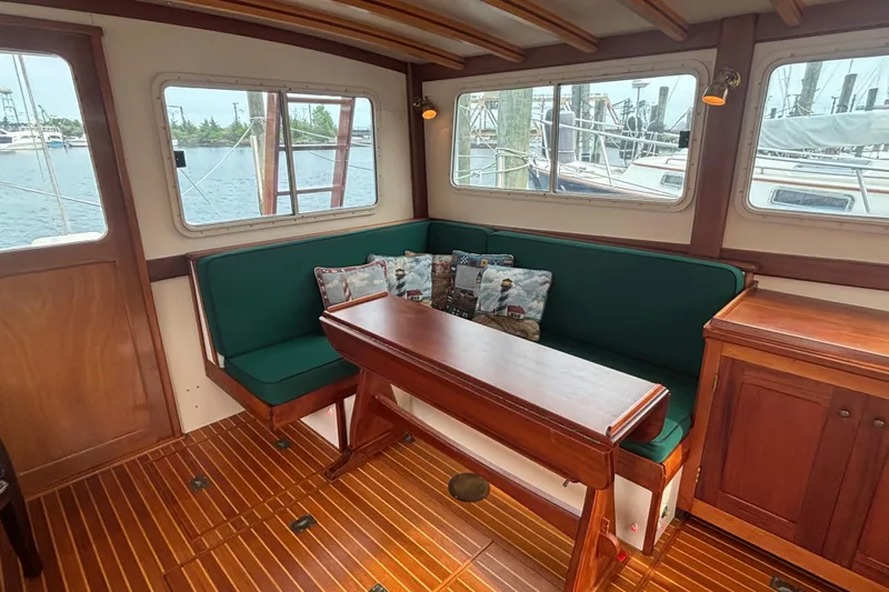 Carroll L Yacht Photos Pics Cozy boat interior with green seating, wooden table, and scenic marina view through windows.