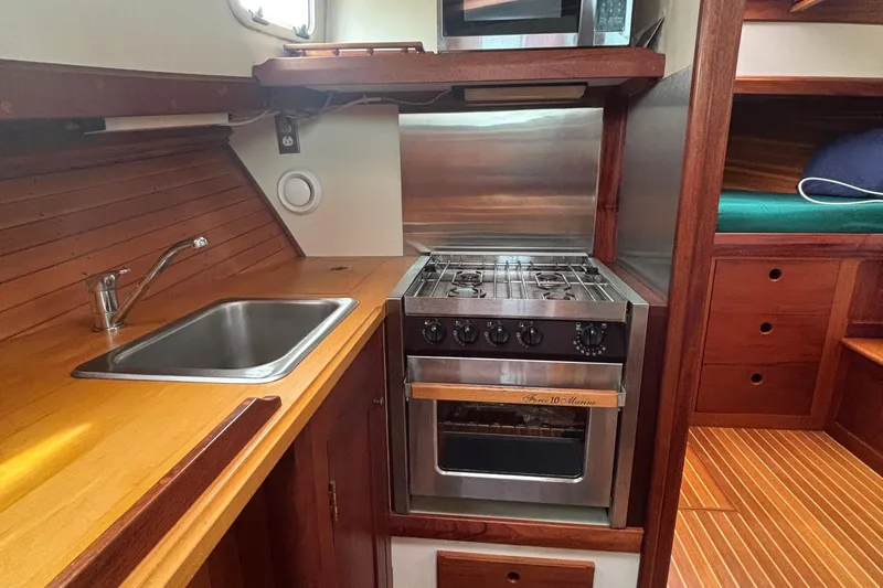 Carroll L Yacht Photos Pics Compact kitchen in a 2001 Lowell 40 boat with stove, sink, and wooden cabinetry.