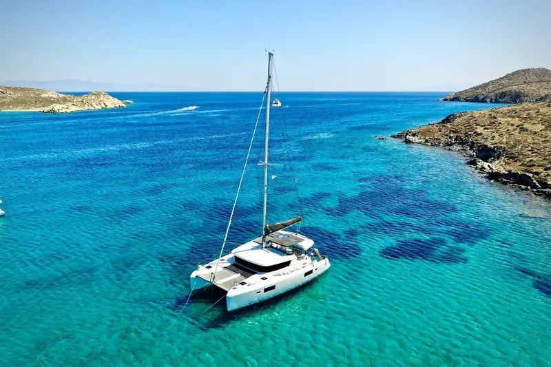 Keyma Yacht Photos Pics 2020 Lagoon 42 catamaran sailing in clear turquoise waters near rocky coastline.