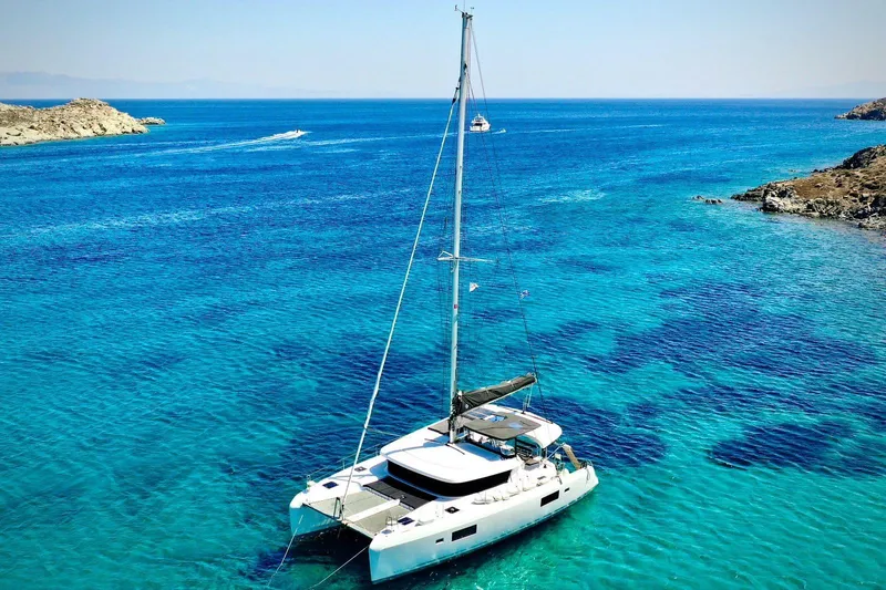 Keyma Yacht Photos Pics 2020 Lagoon 42 catamaran sailing in clear turquoise waters near rocky coastline.