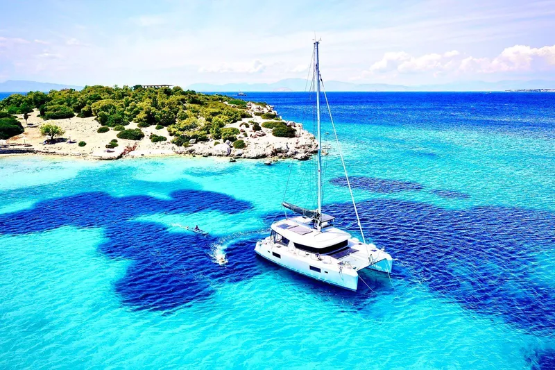 Keyma Yacht Photos Pics Lagoon 42 catamaran sailing in crystal-clear turquoise waters near a scenic island, 2020 model.