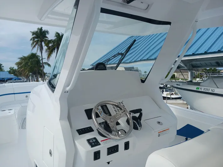  Yacht Photos Pics 2024 Intrepid 375 Nomad SE boat helm with steering wheel and controls, docked near palm trees.