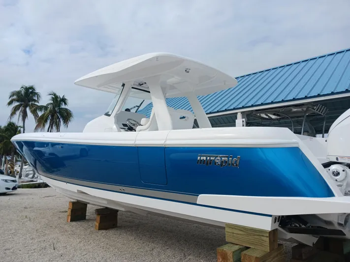  Yacht Photos Pics 2024 Intrepid 375 Nomad SE boat with blue hull, displayed outdoors on wooden blocks.