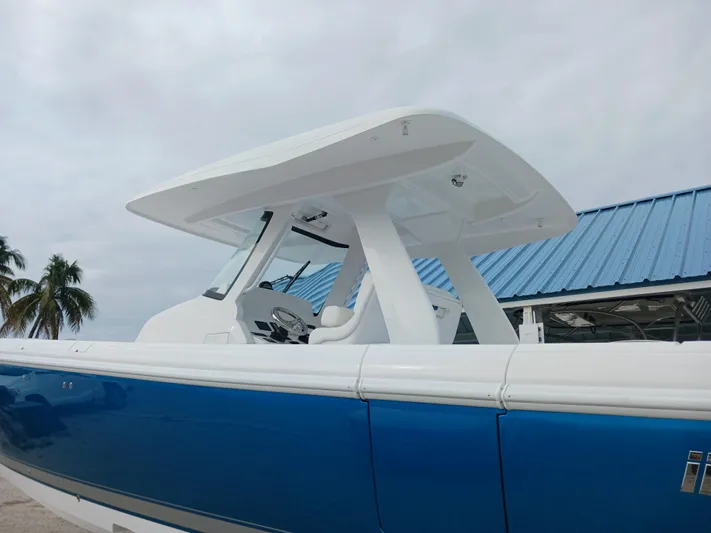  Yacht Photos Pics 2024 Intrepid 375 Nomad SE boat with blue hull and white top, docked near palm trees.